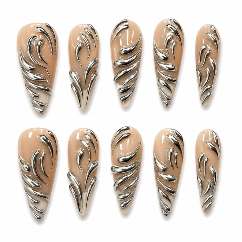 Ten coffin-shaped press-on nails arranged in two rows of five on a plain white background. Each nail has a glossy nude-beige base with raised metallic silver leaf-like swirl patterns.