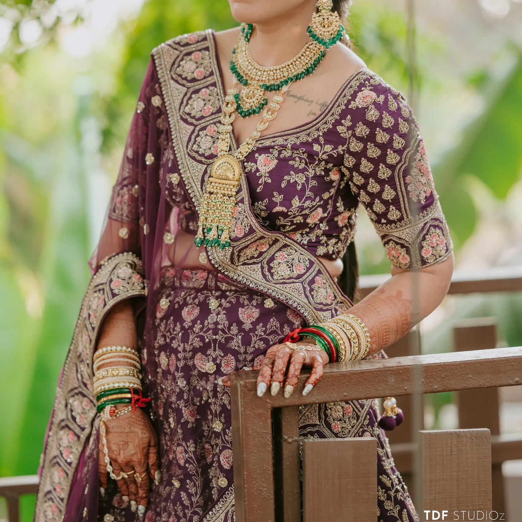 Woman in traditional attire with jewelry, standing outdoors with greenery in the background