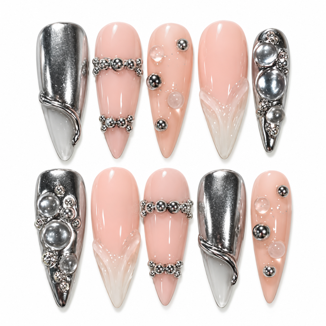 Ten pointed-toe press-on nails arranged in two rows on a white background. The nails feature a mix of metallic silver designs, pale pink and white gradient designs, and embellishments with silver beads, pearls, and rhinestones.