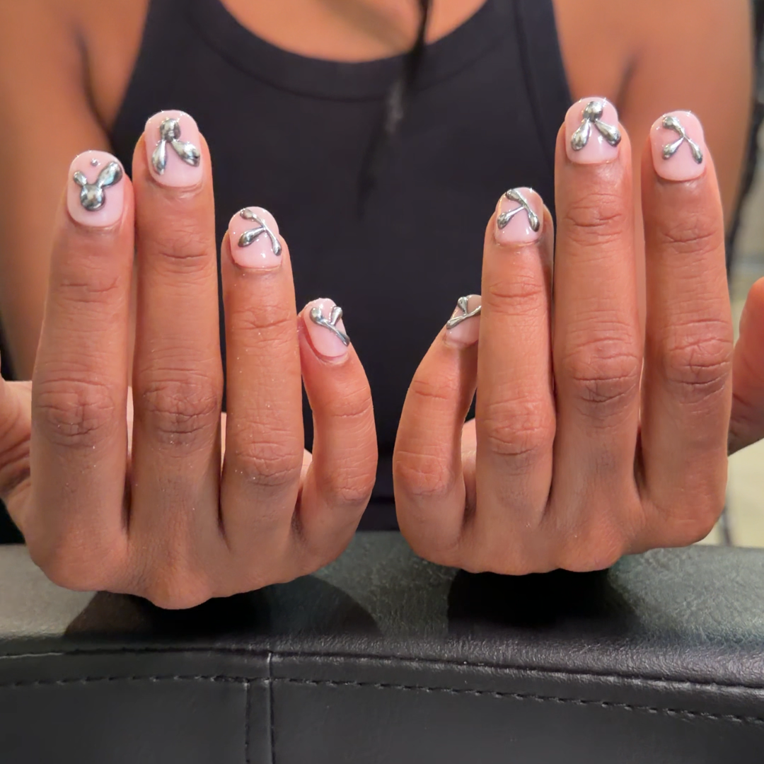 A close-up of a person's hands displaying a manicure with white base polish and delicate floral designs, with the brand name 'Oxalis Bliss' visible on a box in the foreground.