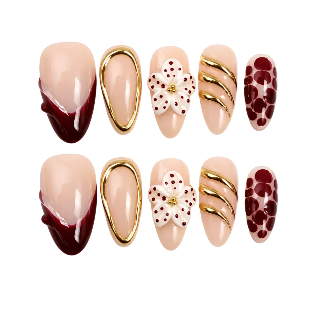 Six-piece press-on nail set arranged in two rows of three on a plain white background. The nails have a glossy nude-peach base with decorative designs including dark burgundy French tips, gold metallic swirls, a white flower with red dots, and a burgundy polka-dot pattern.