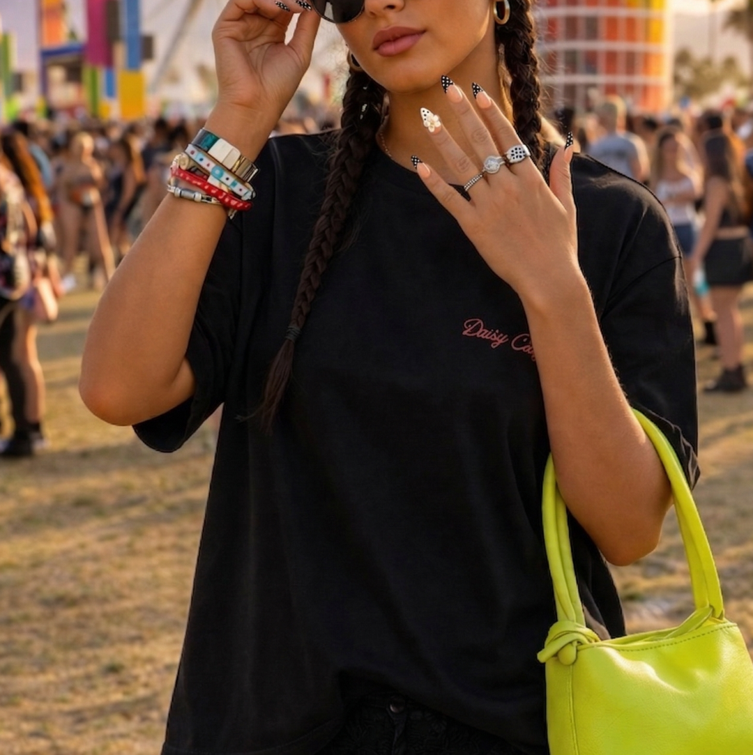 Woman at a music festival wearing sunglasses and a black outfit with a yellow bag, ferris wheel in the background.