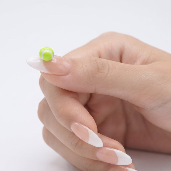 A close-up of a hand with long, almond-shaped French manicure nails, holding a small round green bead on a clean white background.