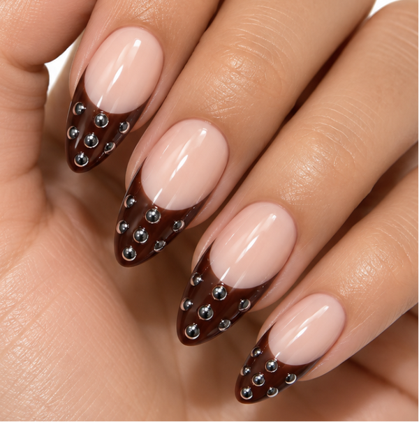 A close-up of a hand showcasing a French manicure with long stiletto-shaped nails. The nails feature a glossy pale pink base, a dark brown French tip, and small silver rhinestone accents along the tip.